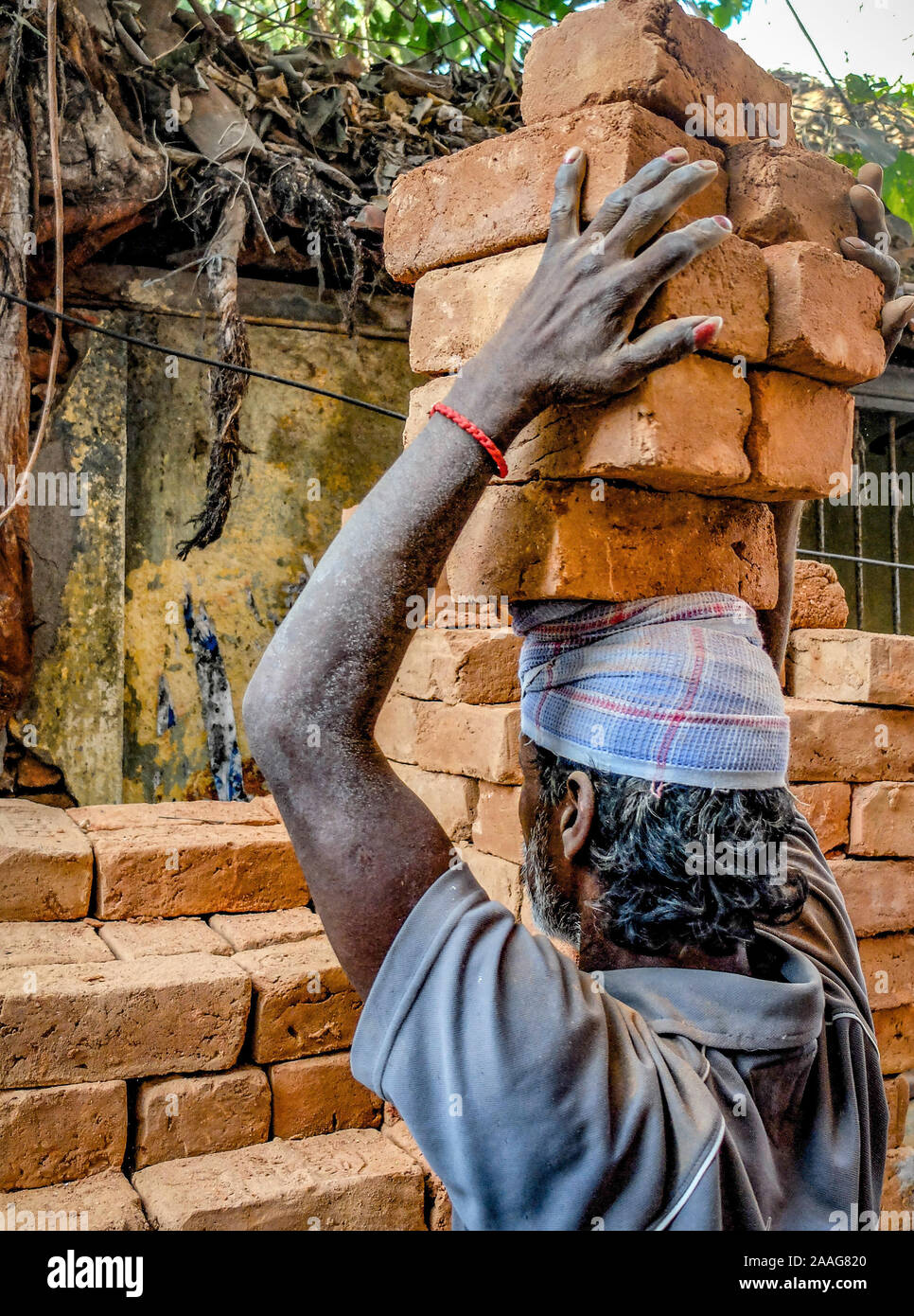 CHENNAI,TAMIL NADU/India-IL 2 MARZO 2018:un operaio carica un peso elevato di mattoni di edificio sulla sua testa in corrispondenza di una piccola casa sito in costruzione. Foto Stock