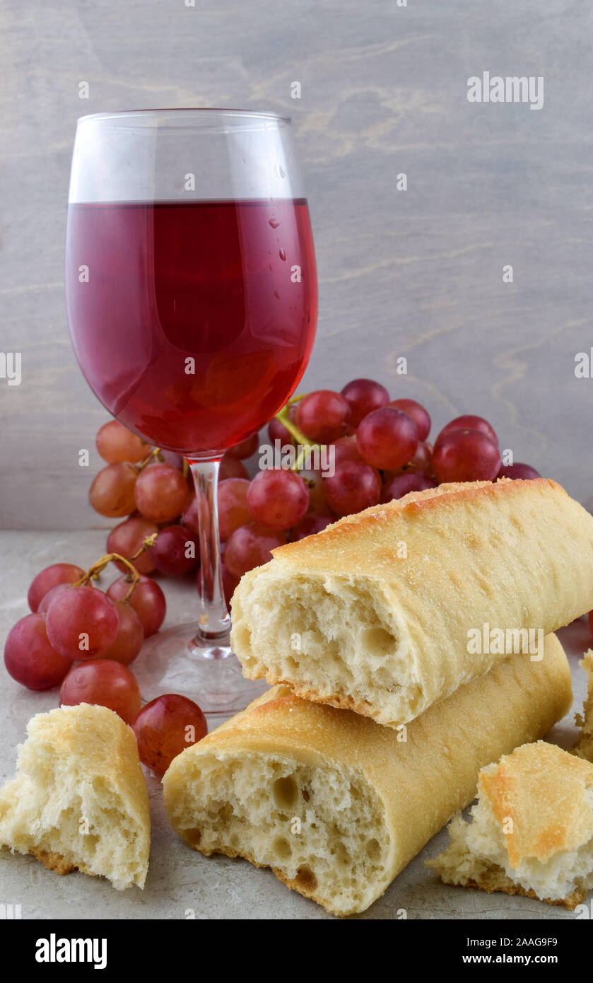 Freschi di forno pane francese, delizioso vino rosso e fresche Uve Rosse sulla cima di una pietra grigia sullo sfondo. Foto Stock