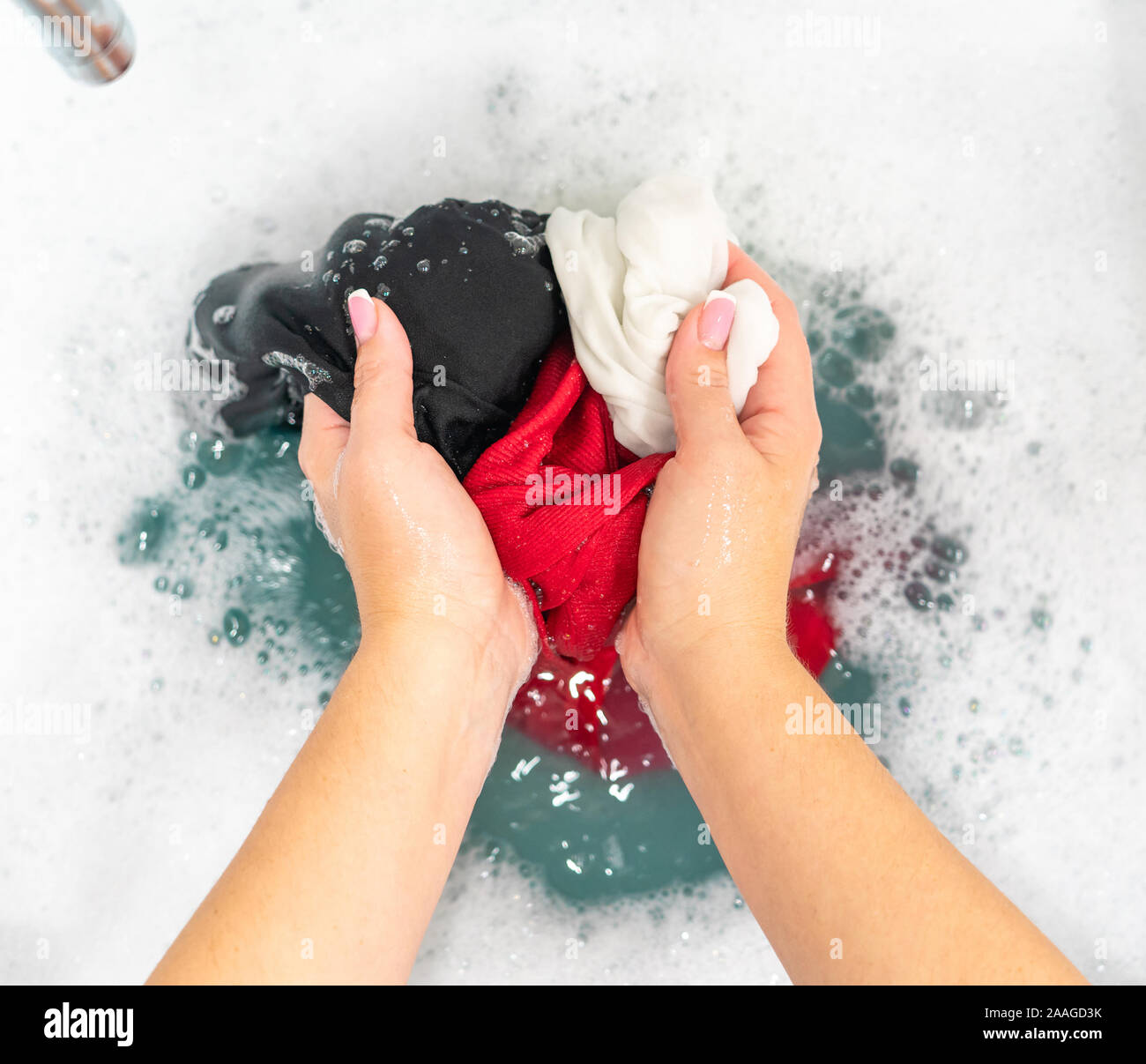 Mani femminili il lavaggio di vestiti di colore nel bacino Foto Stock