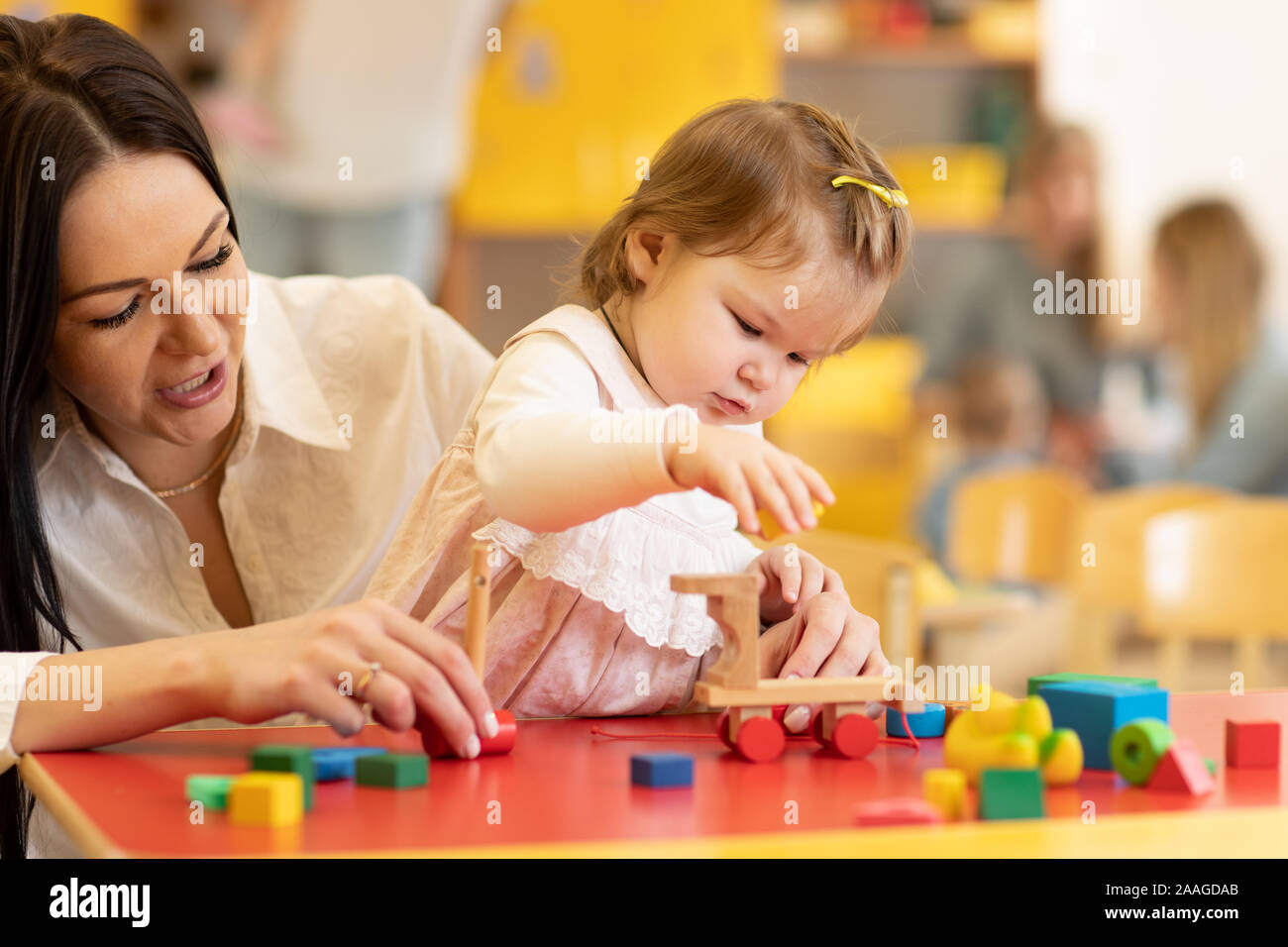 Piccolo bambino caucasico ragazza che gioca con il giocattolo Montessori in pre-scuola. Donna capretto di insegnamento in una scuola materna Foto Stock