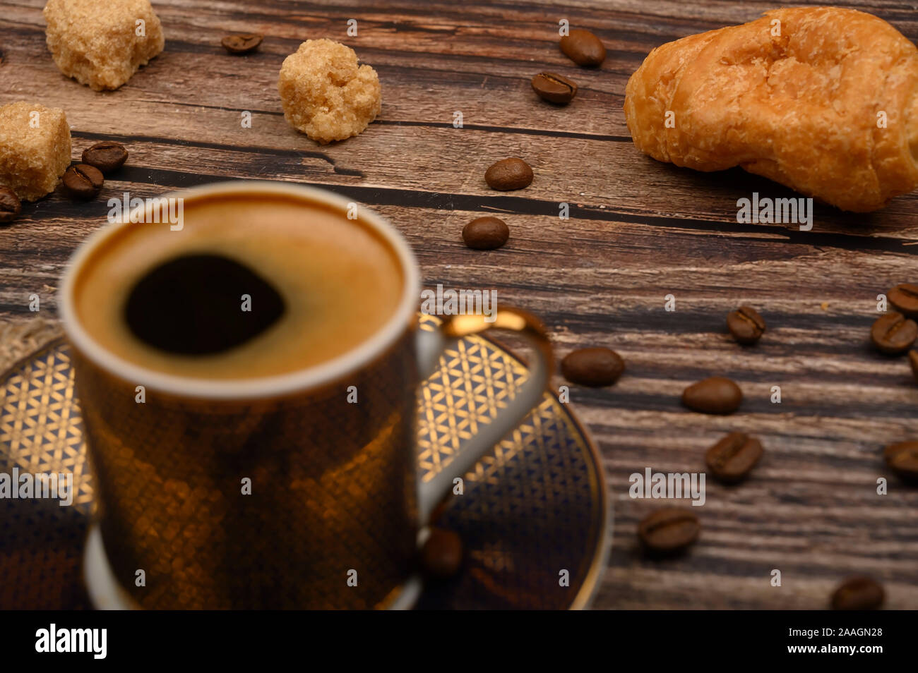 Tazza da caffè, croissant, lo zucchero di canna e i chicchi di caffè su sfondo di legno. Close up Foto Stock