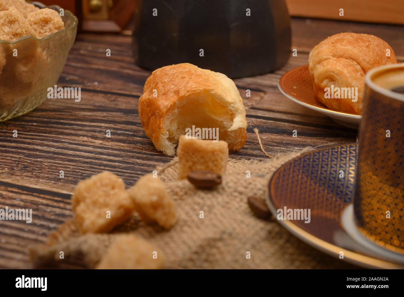 Pezzi di zucchero di canna, croissant e una tazza di caffè su un sfondo di legno. Close up Foto Stock