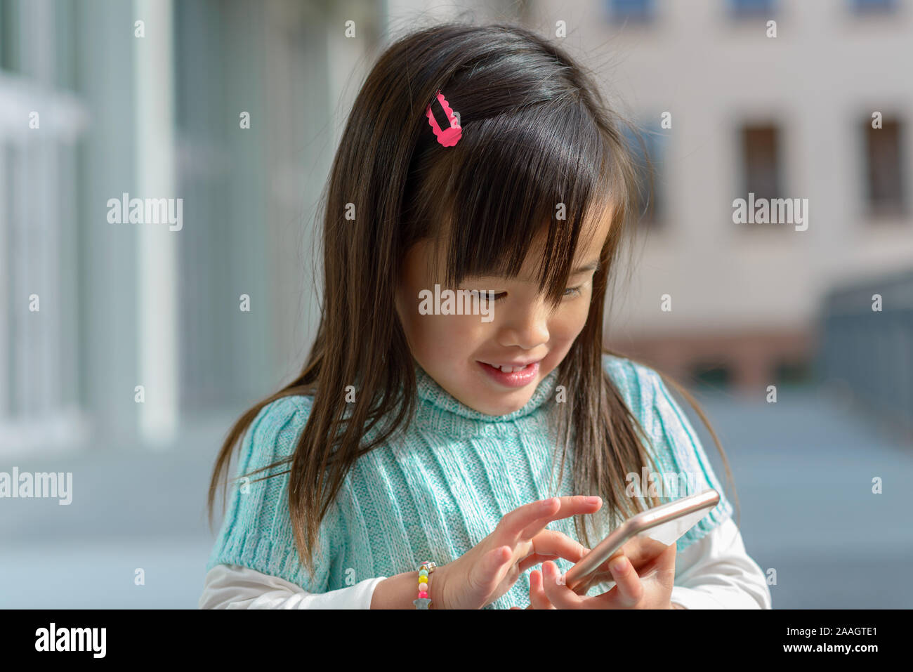 Piuttosto alla moda bambina gioca con un telefono cellulare all'aperto sotto il sole sorride mentre naviga sullo schermo Foto Stock