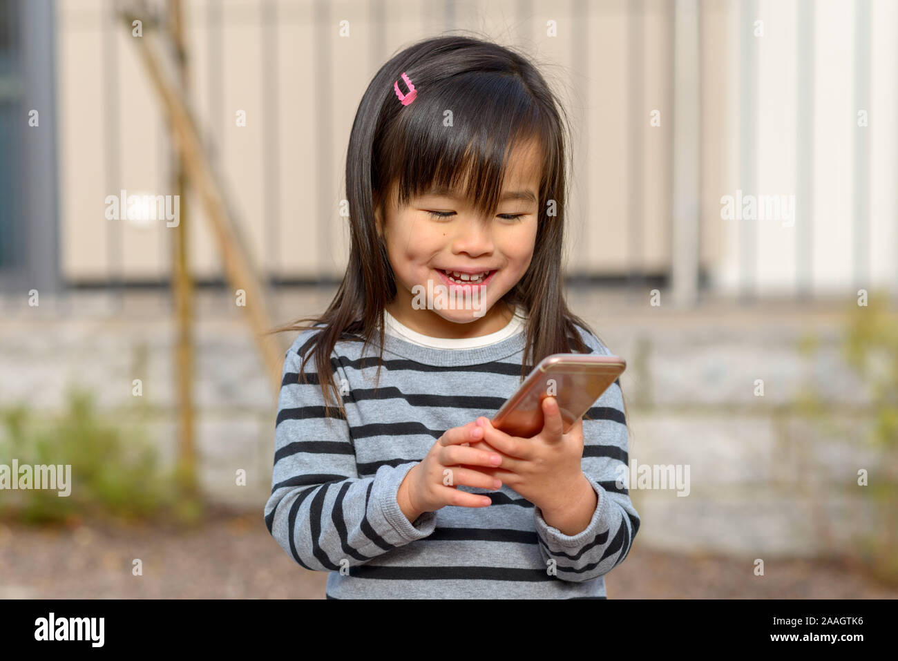 Carino bambina affascinato da un telefono cellulare seduti all'aperto la lettura dello schermo con un espressione assorti Foto Stock