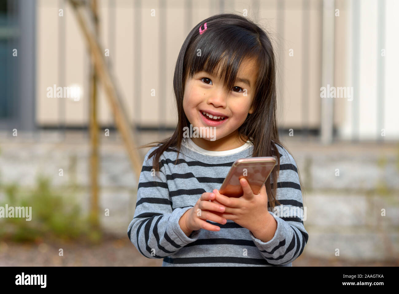 Felice vivace bambina in possesso di un telefono cellulare all'esterno guardando la telecamera con un sorriso raggiante di piacere Foto Stock