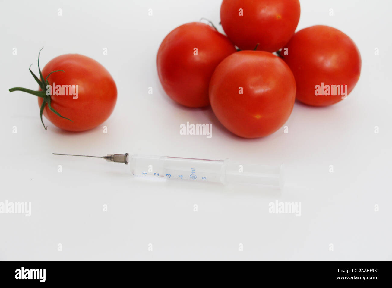 Siringa e pomodori. Su uno sfondo luminoso sono il rosso dei pomodori e una siringa. Nessuno. Geneticamente Modificati concetto nutrizionale. Foto Stock