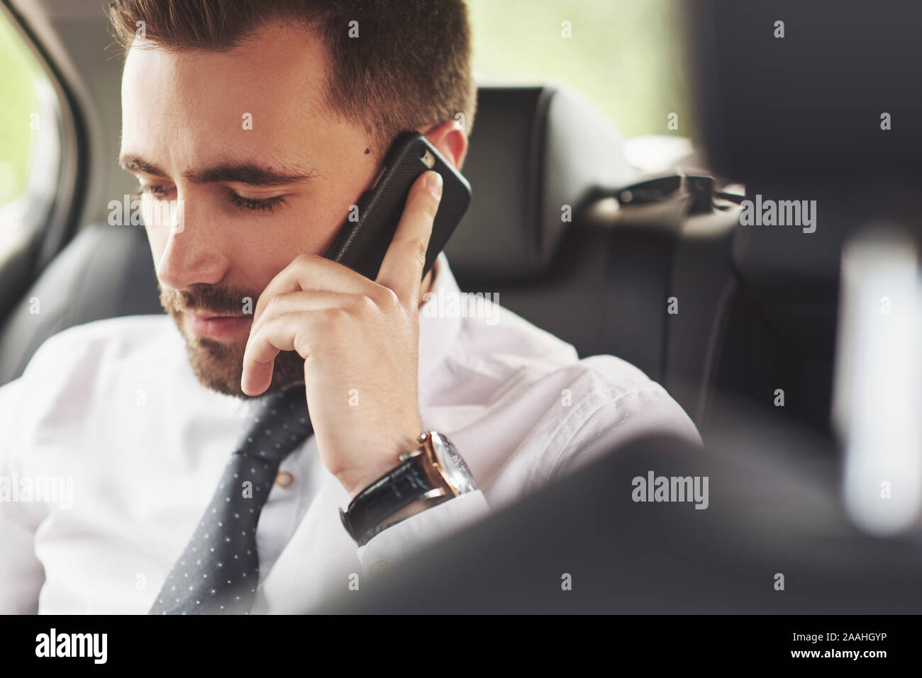 Un imprenditore che invia un messaggio a uno smartphone e va al sedile posteriore della vettura. Foto Stock