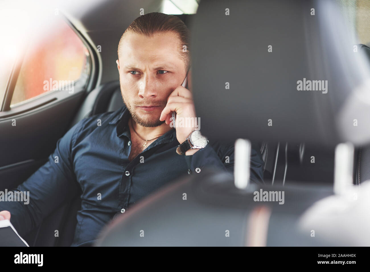 Un imprenditore che invia un messaggio a uno smartphone e va al sedile posteriore della vettura. Foto Stock