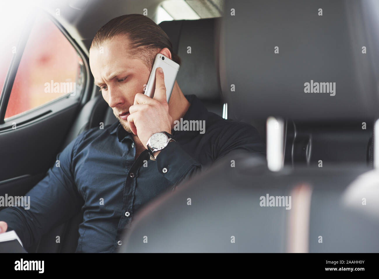 Un imprenditore che invia un messaggio a uno smartphone e va al sedile posteriore della vettura. Foto Stock