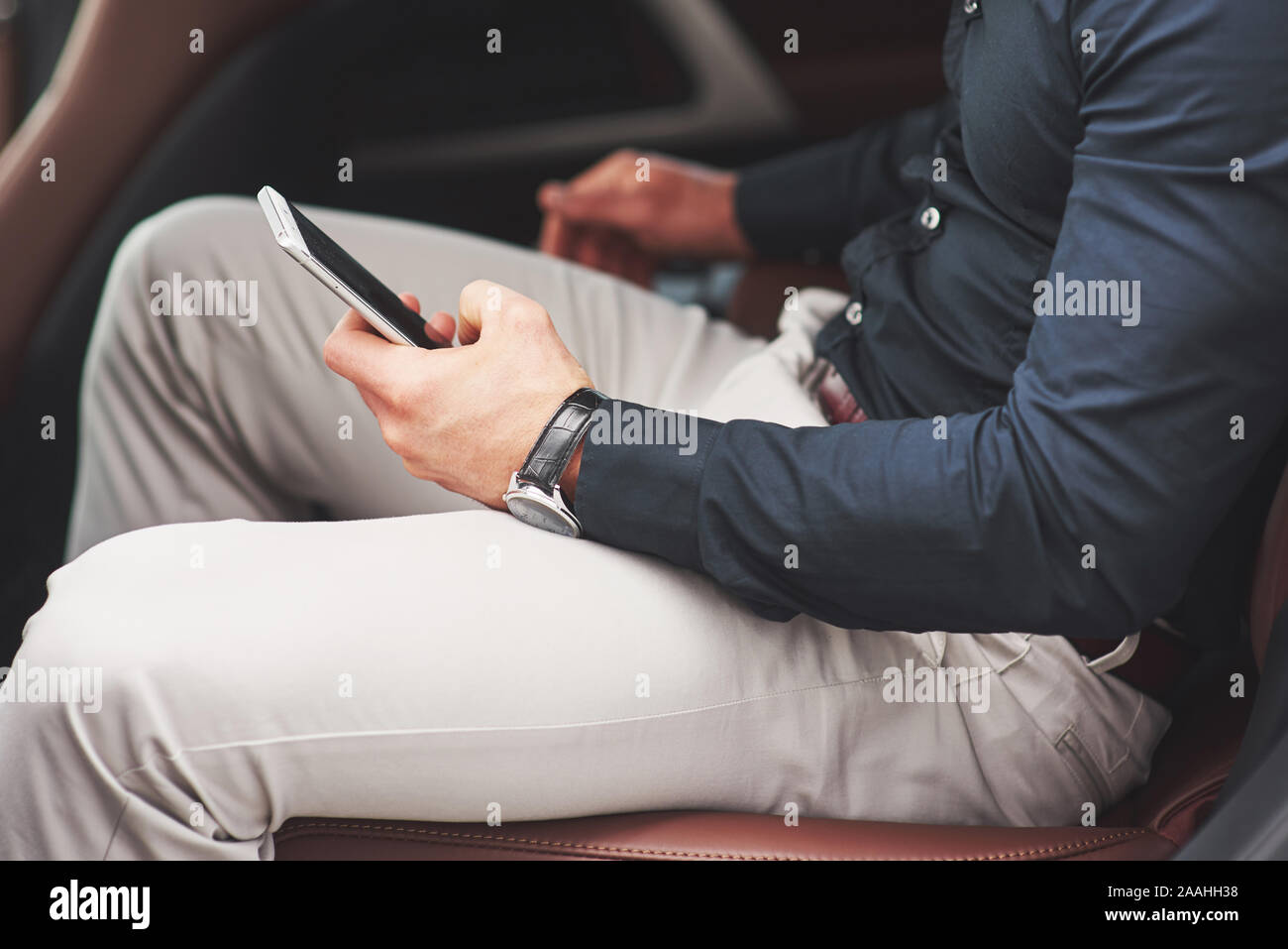 Un imprenditore che invia un messaggio a uno smartphone e va al sedile posteriore della vettura. Foto Stock