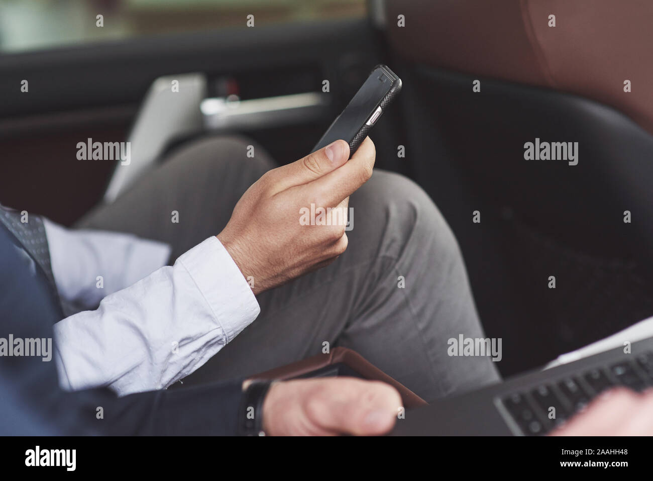 Un imprenditore che invia un messaggio a uno smartphone e va al sedile posteriore della vettura. Foto Stock
