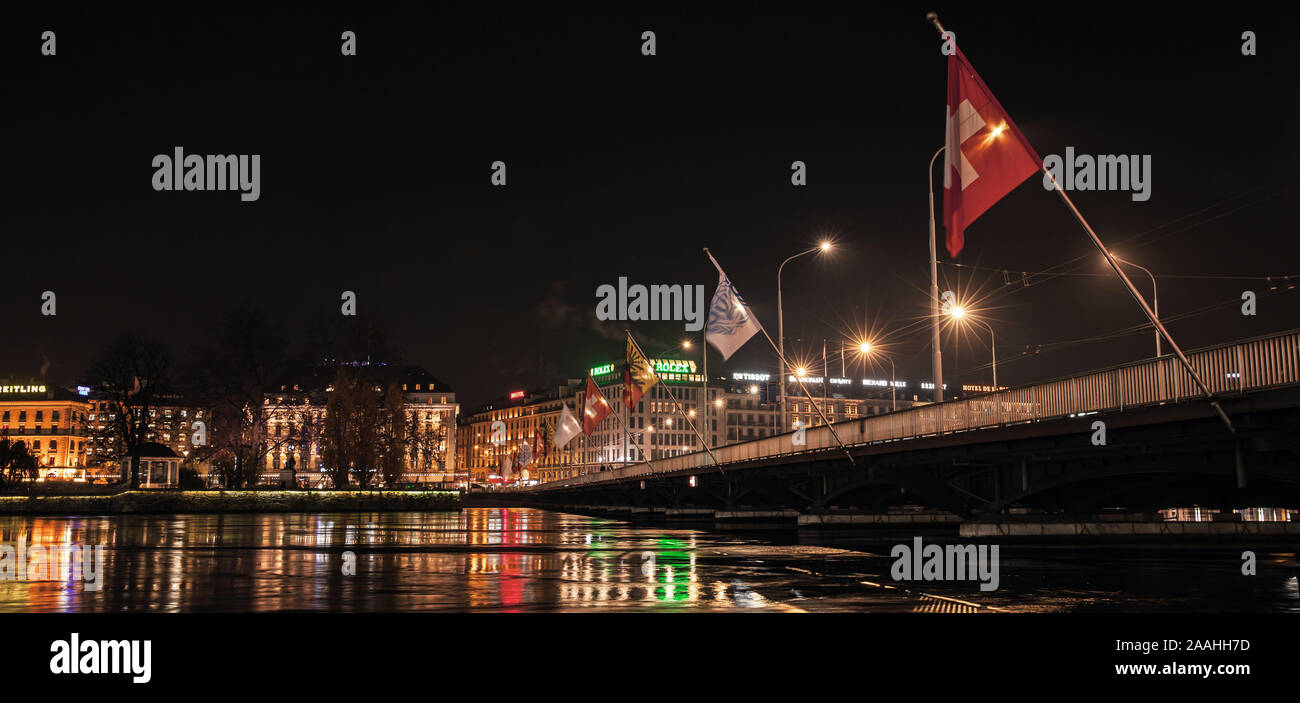 Ginevra, Svizzera - 24 Novembre 2016: Panoramica notte cityscape con la bandiera svizzera e facciate illuminate su un lungo fiume nella zona centrale di Ginevra ci Foto Stock