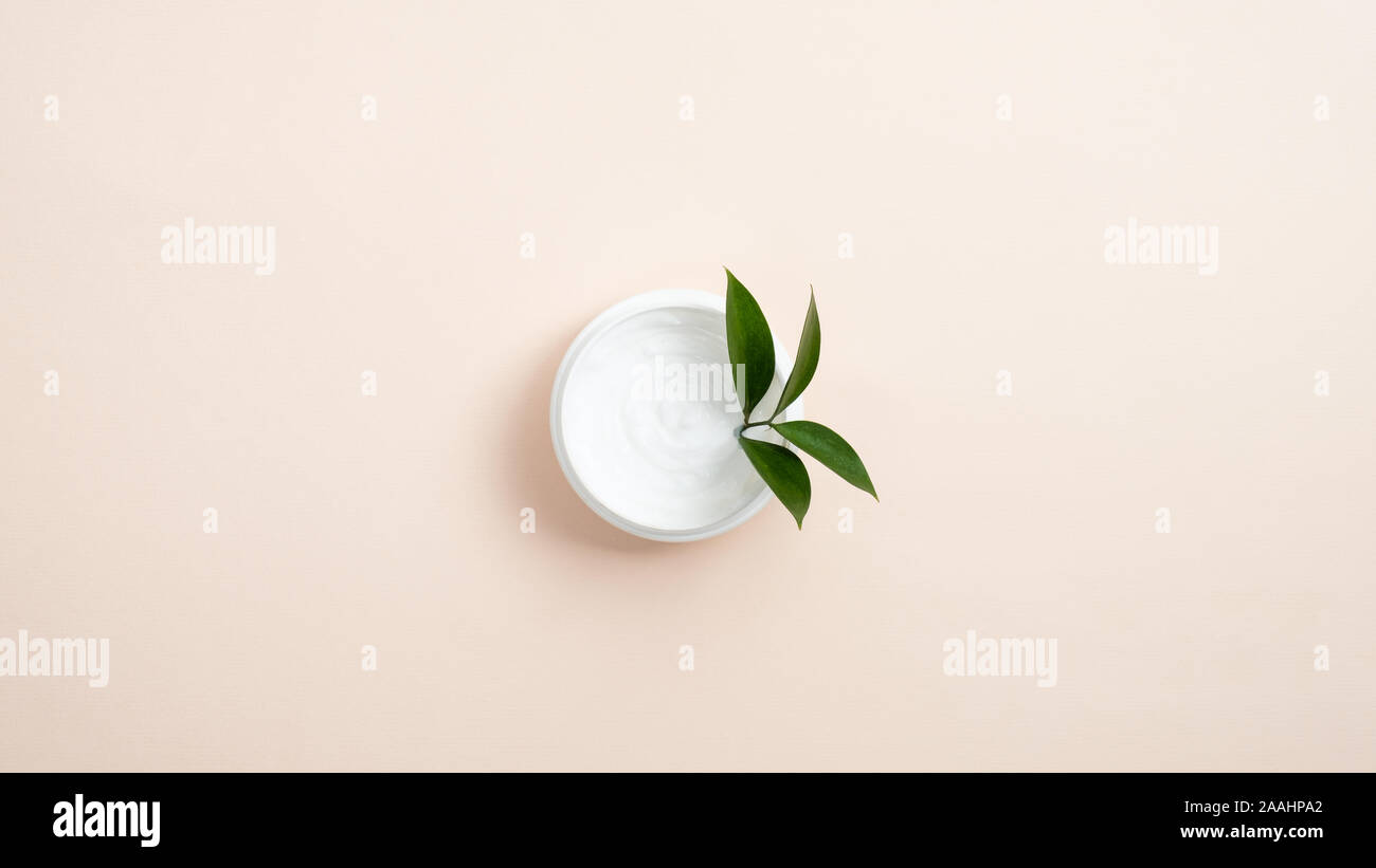 Vaso con organici bianco crema cosmetica e foglia verde pastello su sfondo beige. Il minimo piatto stile laici composizione, vista dall'alto. La cura della pelle e servizi sanitari Foto Stock