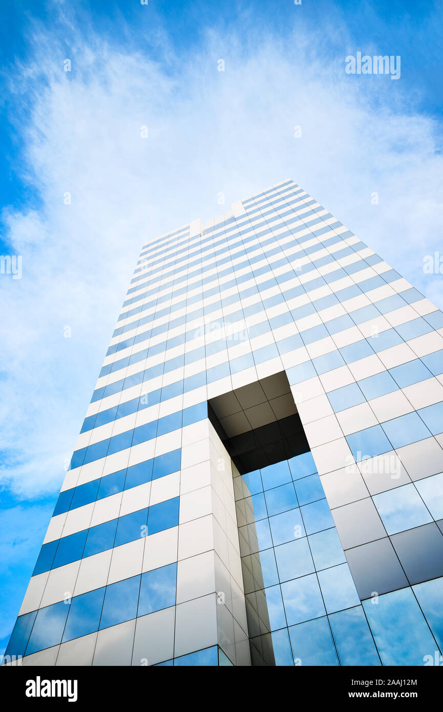 La parte superiore di un moderno grattacielo o edificio commerciale con finestre di vetro e cielo blu con nuvole in background Foto Stock
