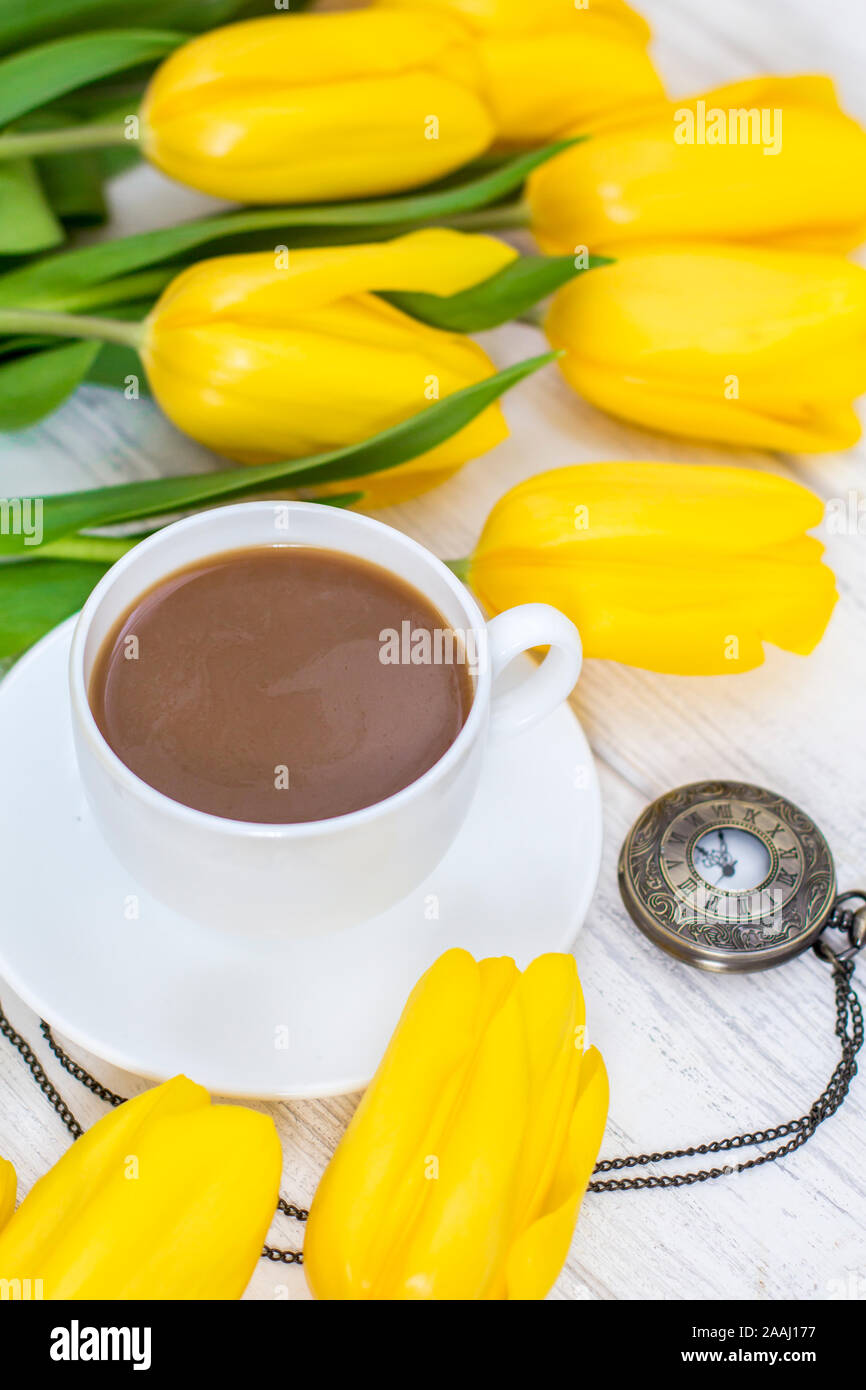 Tulipani gialli, una tazza di caffè, cappuccino e vintage guarda su una catena su un bianco sullo sfondo di legno Foto Stock