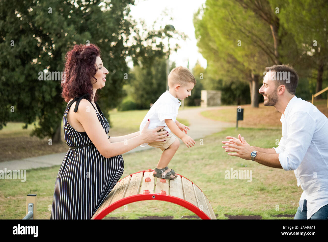 I genitori giocando con il figlio in oscillazione circolare in posizione di parcheggio Foto Stock