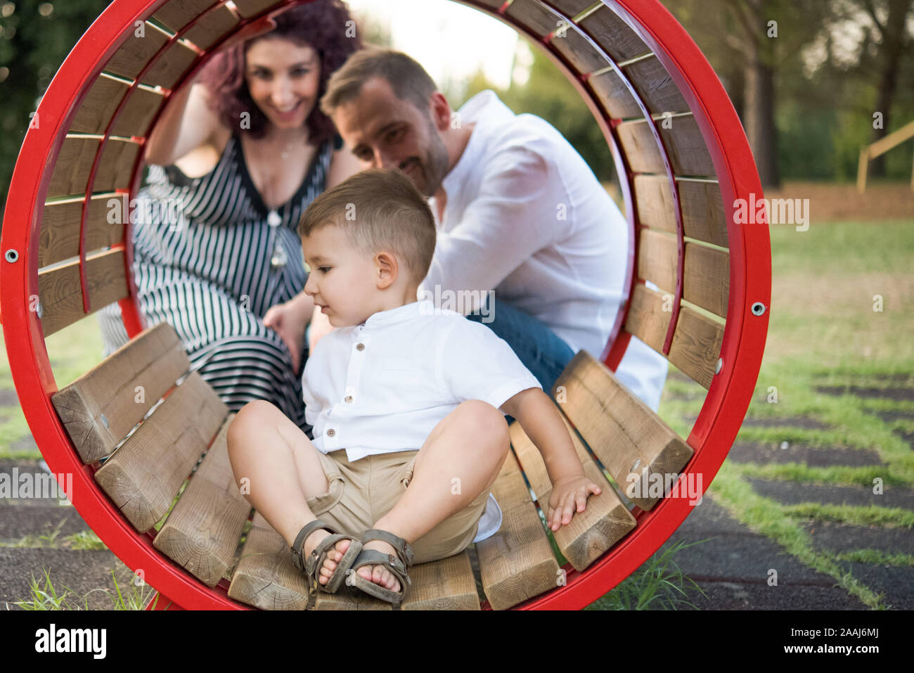 I genitori guardare figlio giocare in oscillazione circolare in posizione di parcheggio Foto Stock