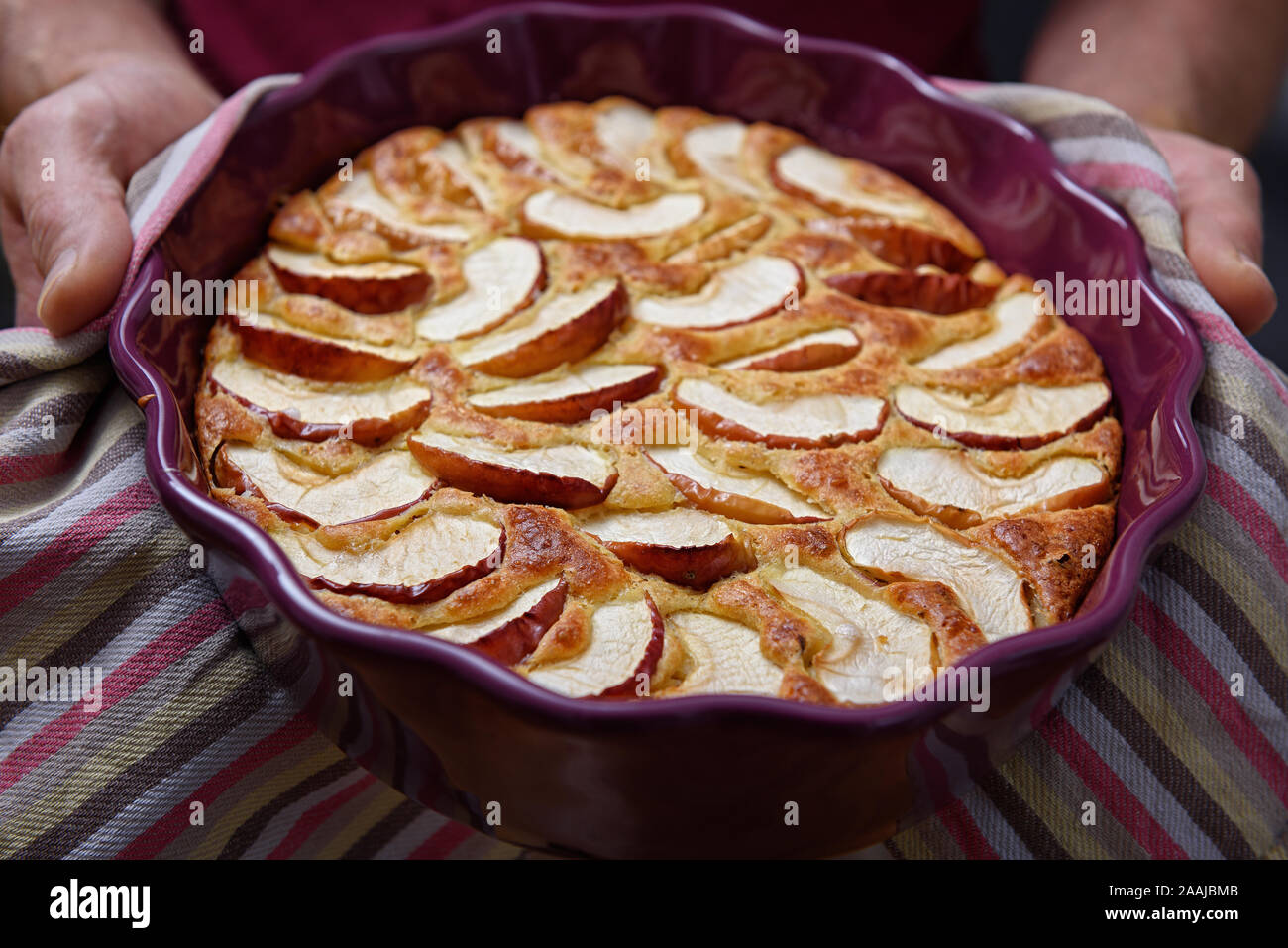 La torta di mele in un recipiente di ceramica. Un uomo è utilizzando un asciugamano per tenere una torta calda. Foto Stock