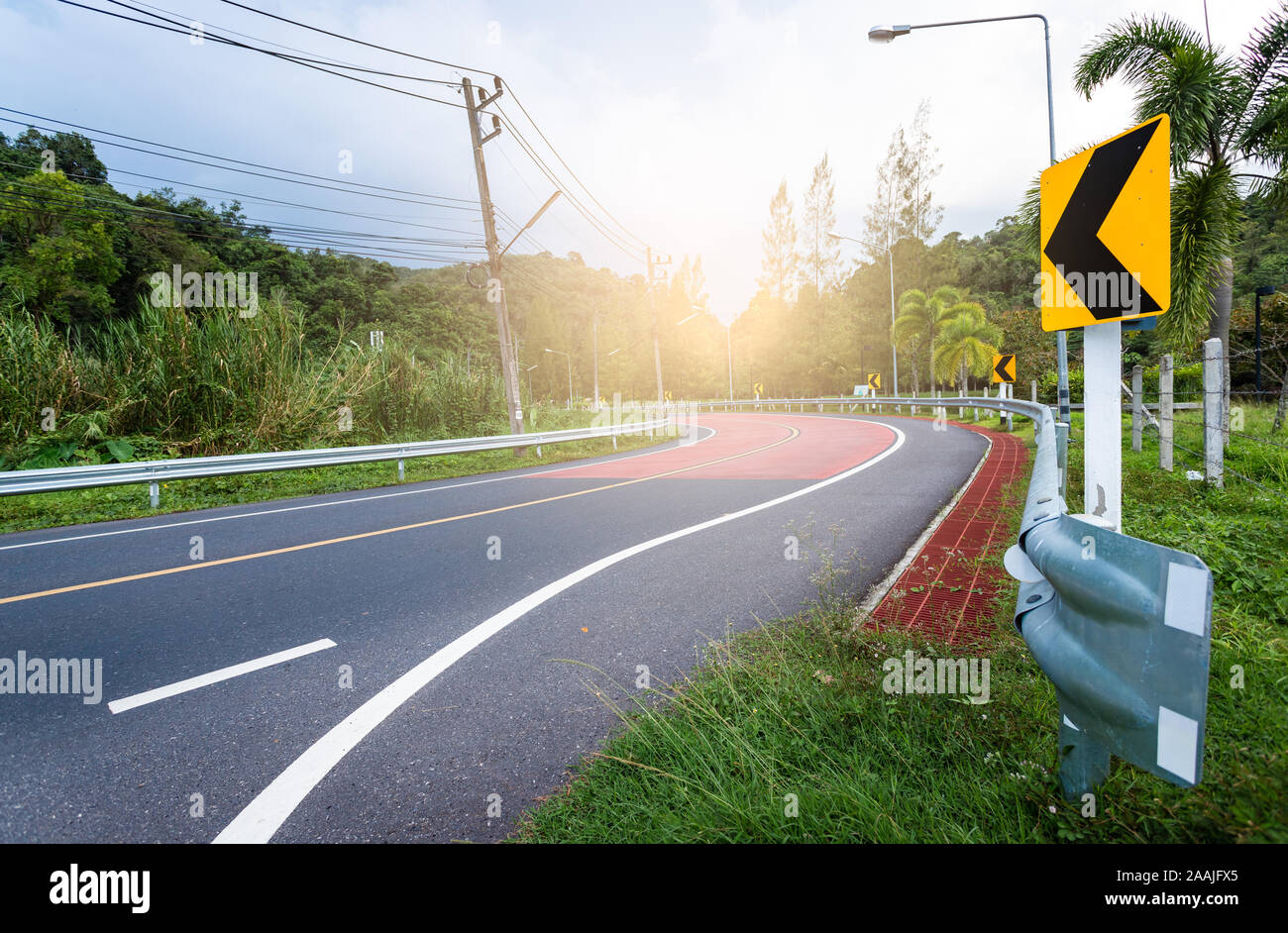 Modo di curva della strada con natura circondano di alberi ed erba, hanno Thai polo elettrico stile, recinzione stradale con il modo montante di guida Foto Stock