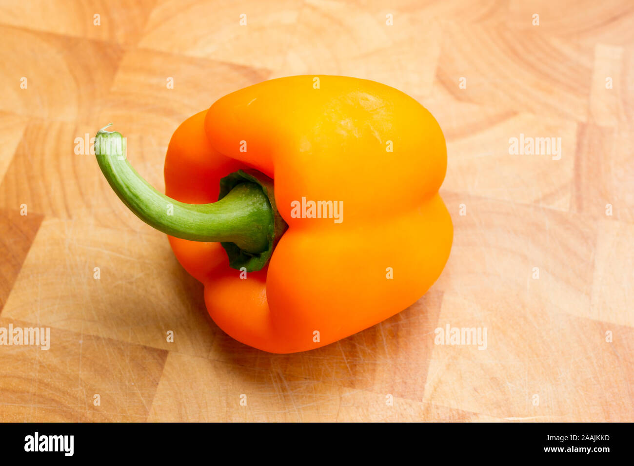 Un peperone d'arancia su un tagliere di legno Foto Stock
