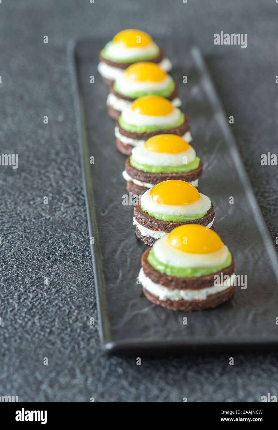 Crostino con crema di formaggio, guacamole fritte e uova di quaglia su piastra Foto Stock