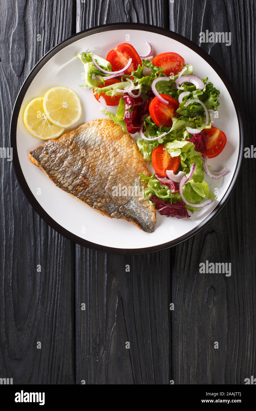Fried orata filetto di pesce con un contorno di insalata di verdure close-up su una piastra sul tavolo. Verticale in alto vista da sopra Foto Stock