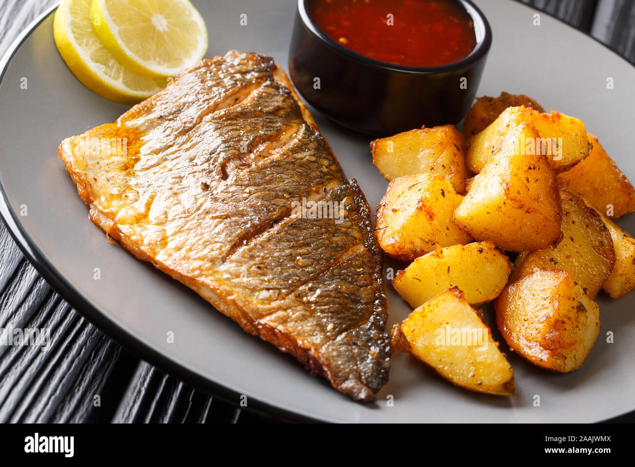 Fried orata filetto di pesce con contorno di patate e salse close-up su una piastra sul tavolo orizzontale. Foto Stock