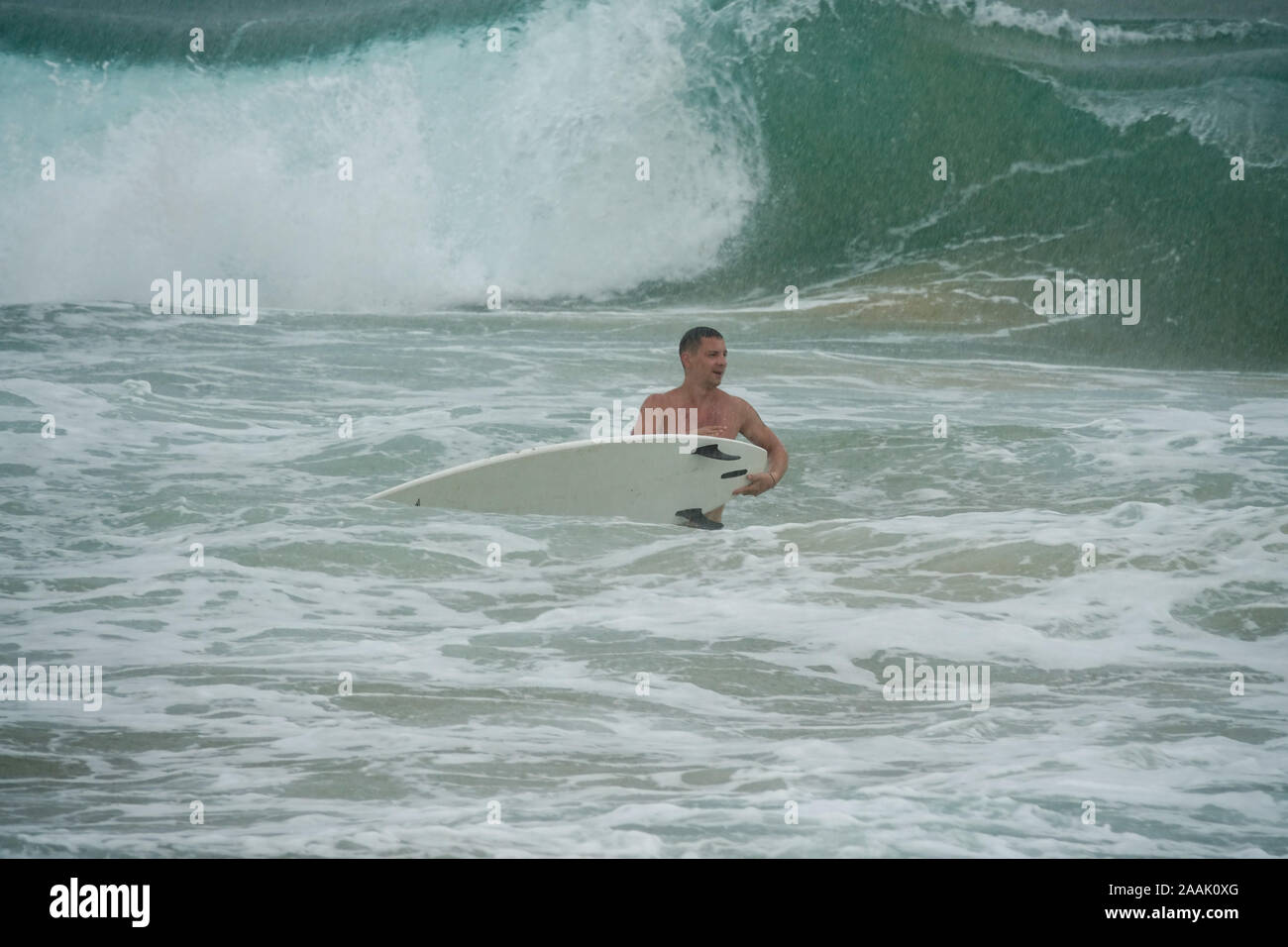 Giovane uomo con la tavola da surf in esecuzione nell'oceano sotto la pioggia Foto Stock