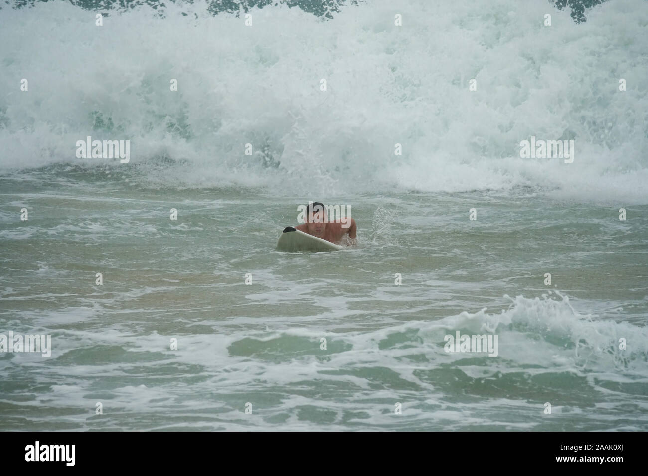 Giovane uomo nuota su una tavola da surf in oceano sotto la pioggia Foto Stock