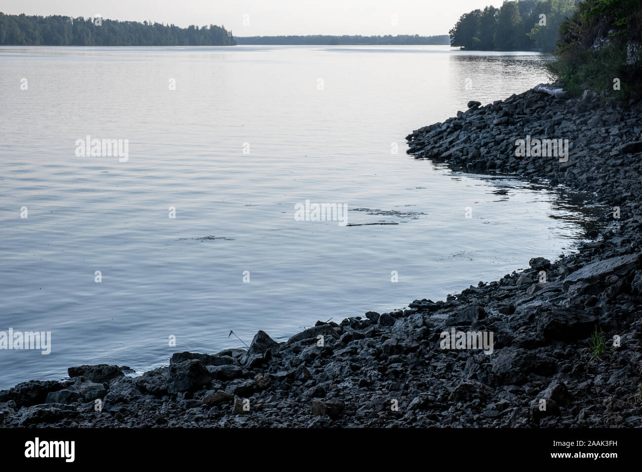 Un avvolgimento rocky riverbank al tramonto. La superficie calma del fiume. Foto Stock