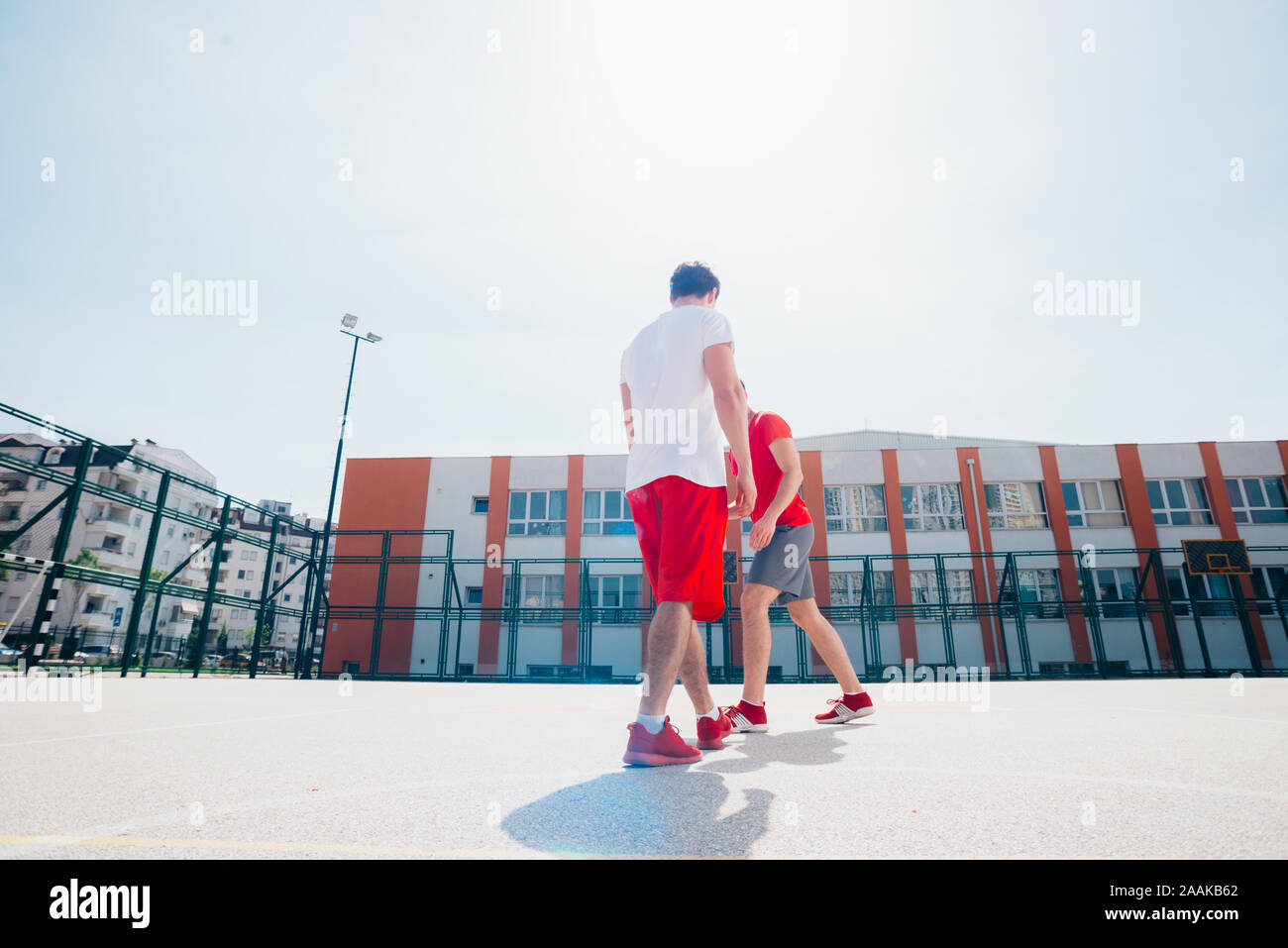 Due amici caucasici indossando rosso dell'apparecchiatura di sport giocando basketballs all'aperto in una giornata di sole mentre essi dribbling e spingere l'altra. Foto Stock