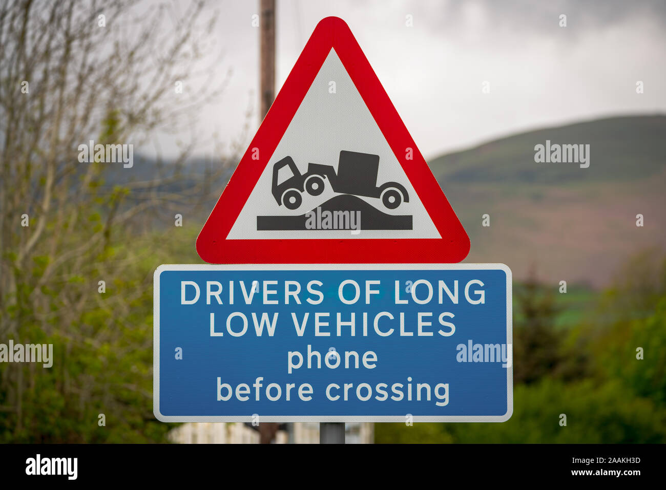 Segno: driver di lunga veicoli basso telefono prima di attraversamento, con sfondo sfocato. Visto in Green Road vicino a trefoli, Cumbria, England, Regno Unito Foto Stock
