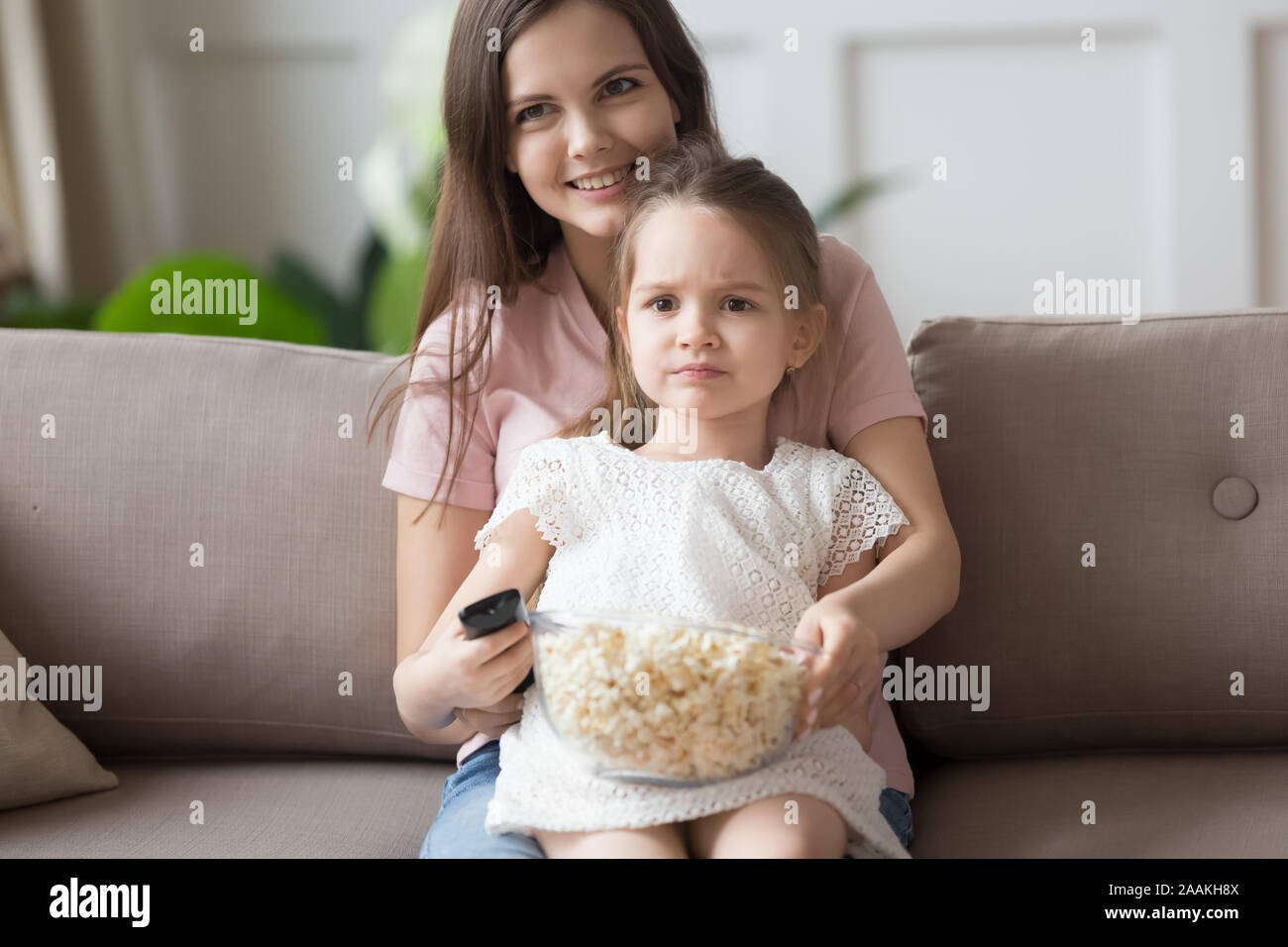 Bambina guarda la TV con il giovane mamma mangiare popcorn Foto Stock