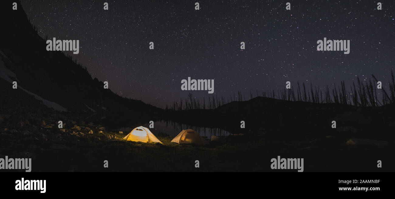 Illuminata tende sulla riva di un alto lago alpino con stelle sopra Foto Stock