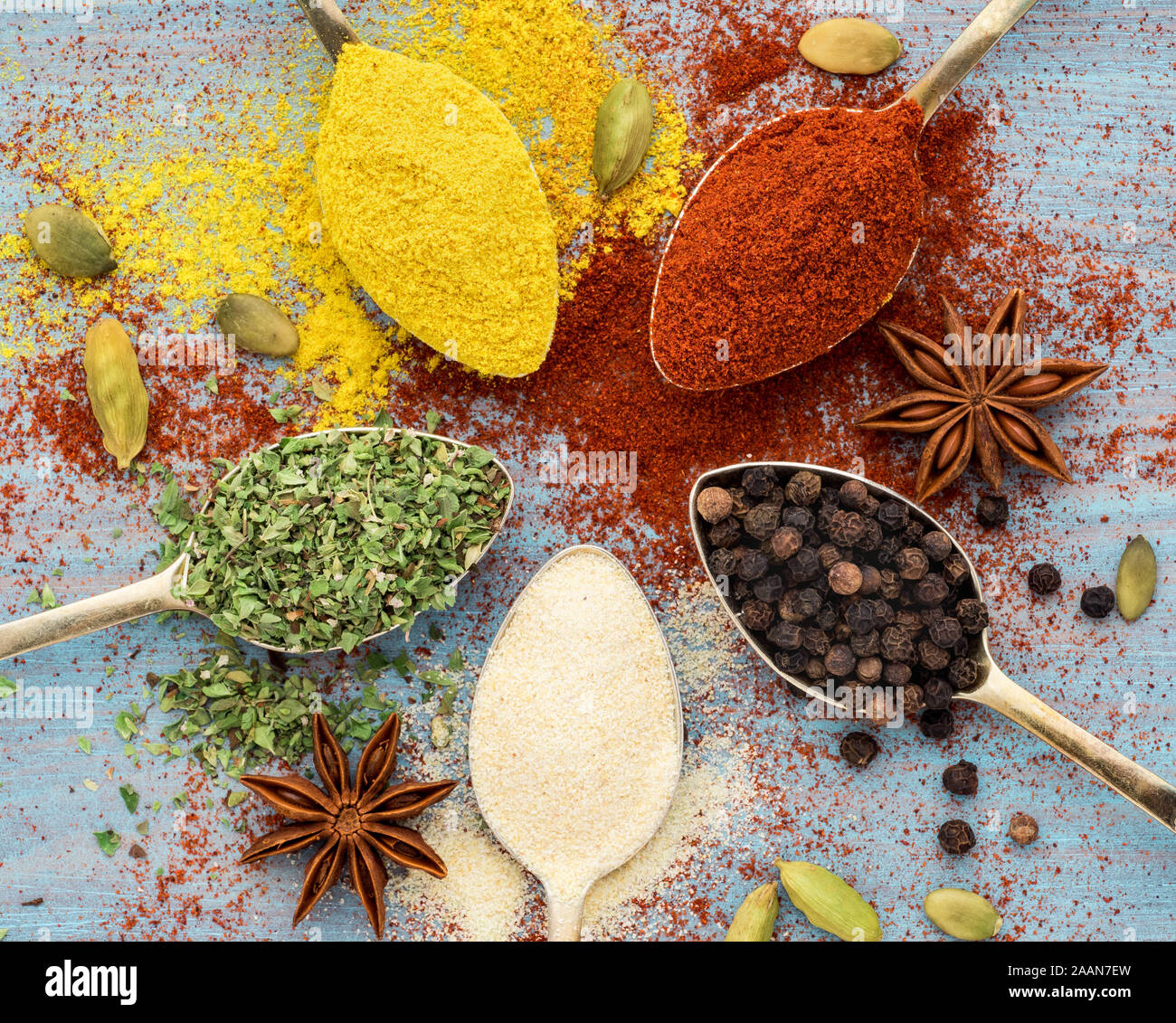 Spezie macinati - aglio, curcuma, paprica, anice, origano, il cardamomo. Round di cucchiai d'oro blu sul tavolo di legno. Vista superiore, close-up Foto Stock