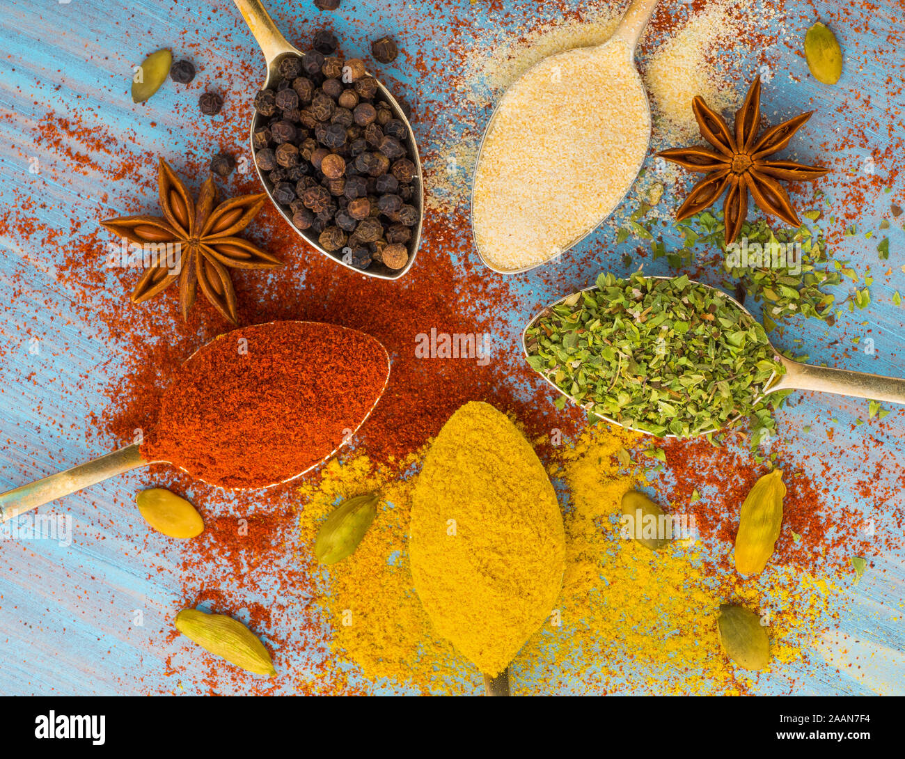 Spezie macinati - aglio, curcuma, paprica, anice, origano, il cardamomo. Round di cucchiai d'oro blu sul tavolo di legno. Vista superiore, close-up Foto Stock