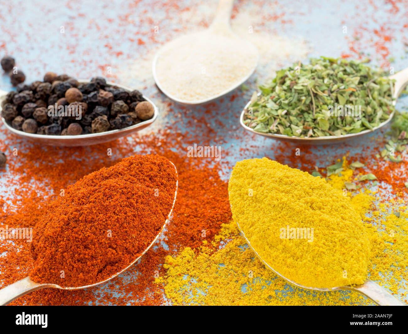 Spezie macinati - aglio, curcuma, paprica, origano. Round di cucchiai d'oro blu sul tavolo di legno. Vista laterale, close-up Foto Stock