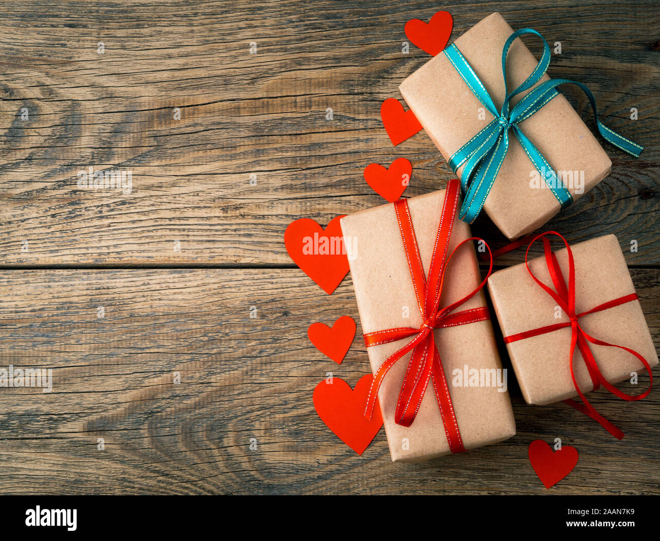 Il giorno di San Valentino sfondo. Doni avvolto con Kraft carta marrone, con nastri rossi, cuori sul rustico invecchiato vintage vecchio sfondo di legno Foto Stock