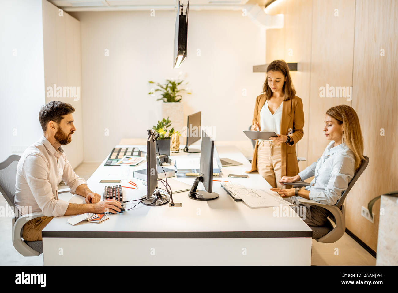 I giovani lavoratori vestito casualmente facendo qualche lavoro creativo al tavolo di grandi dimensioni con i computer in ufficio. Concetto di un patrimonio architettonico di business e il lavoro creativo Foto Stock