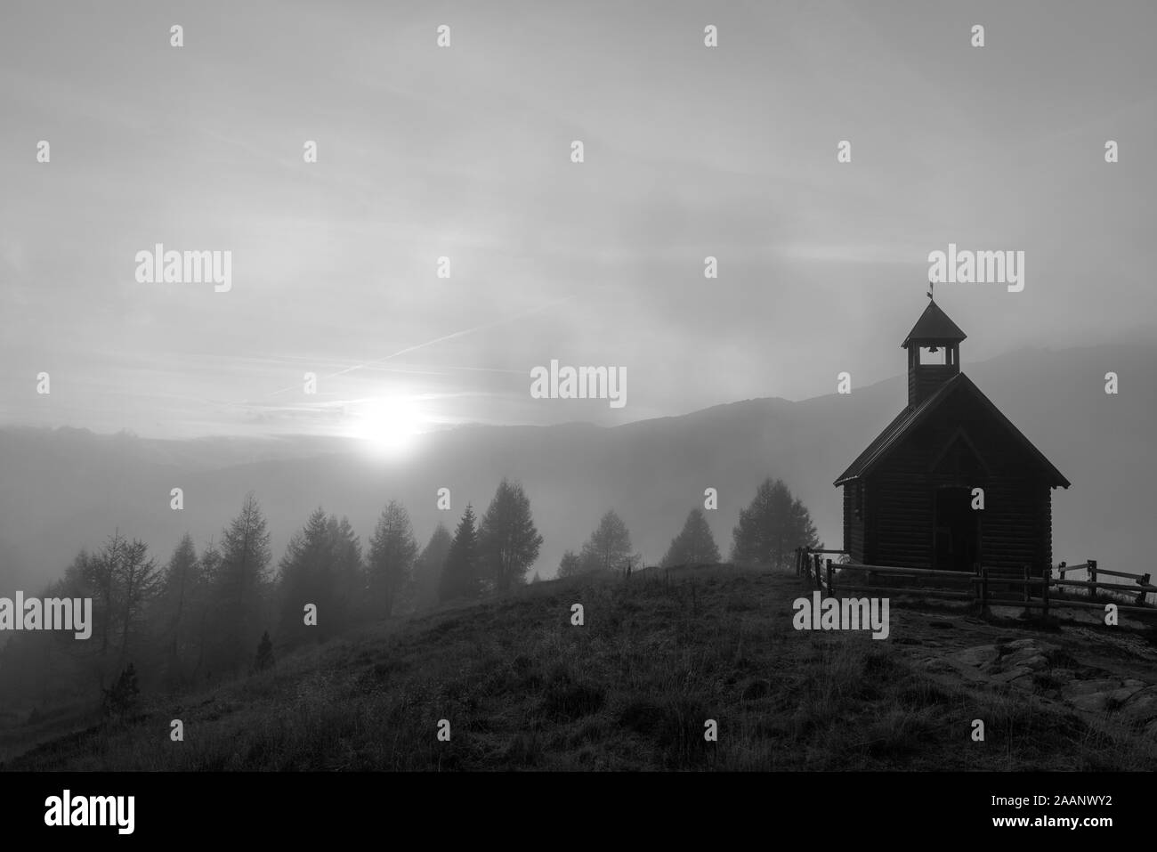 Moody foto in bianco e nero di una piccola cappella su una montagna che si affaccia su una valle di nebbia al tramonto al Passo Valles nelle Dolomiti italiane, perfe Foto Stock