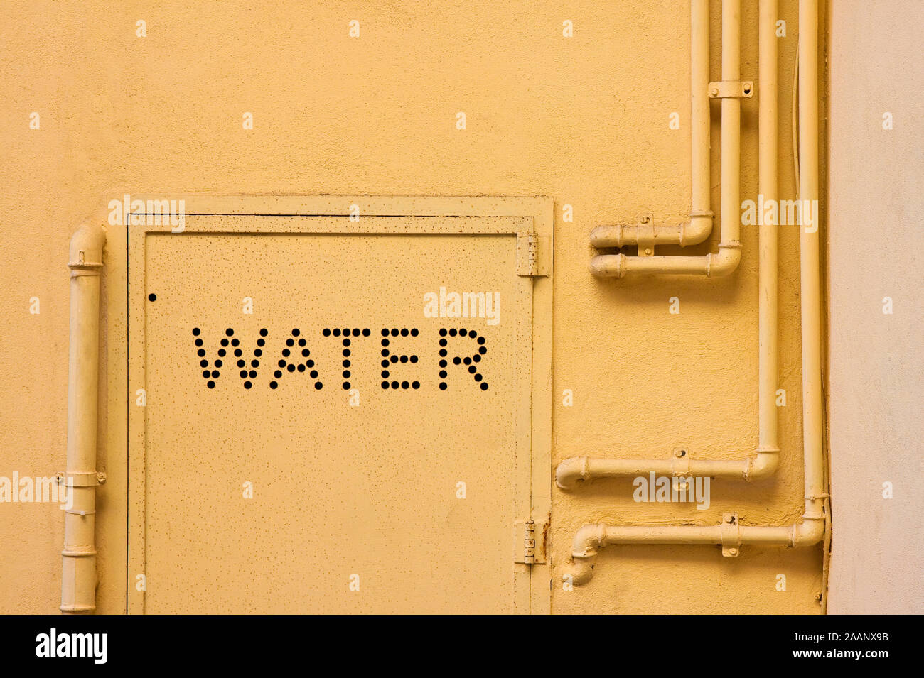 Acqua di vecchi tubi metallici fissati con staffe di fronte ad una parete di gesso con scatola di metallo per misuratore di acqua Foto Stock