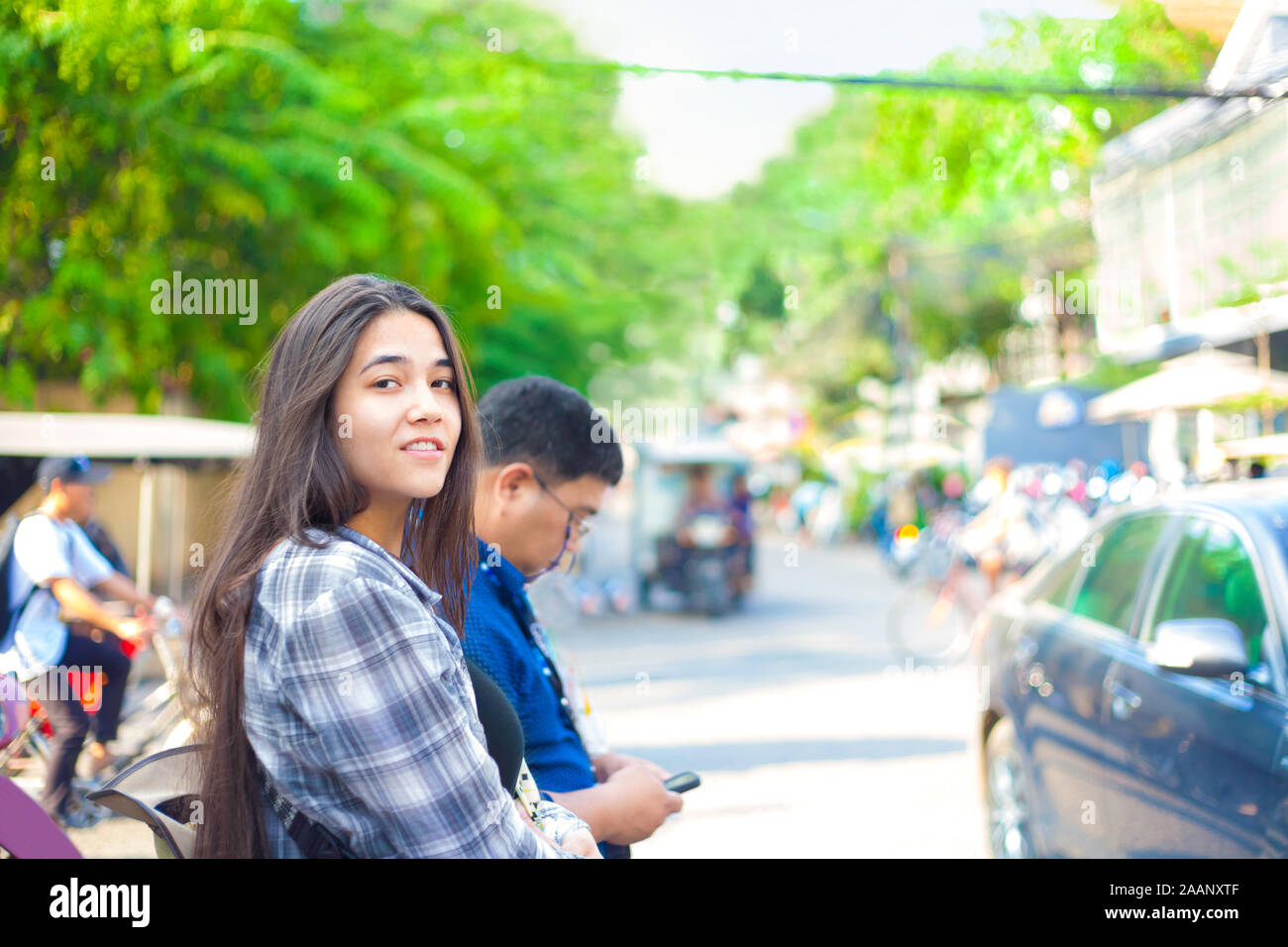 Biracial teen ragazza o donna giovane turista in attesa di taxi per le strade di Phnom Pehn, Cambogia vicino a traffico di tuktuks Foto Stock