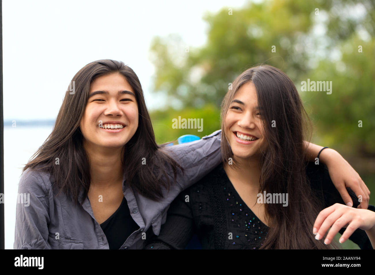 Due sorelle biracial, Asian Caucasian teen ragazze, sorride all'aperto sul lago di Garda con le braccia sopra le spalle Foto Stock