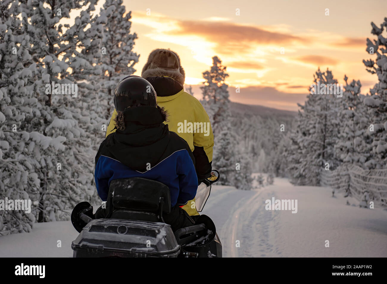 Finlandia, Inari - Gennaio 2019: 2 persone a cavallo su una motoslitta attraverso le selvagge della Lapponia, sotto un cielo rosso Foto Stock