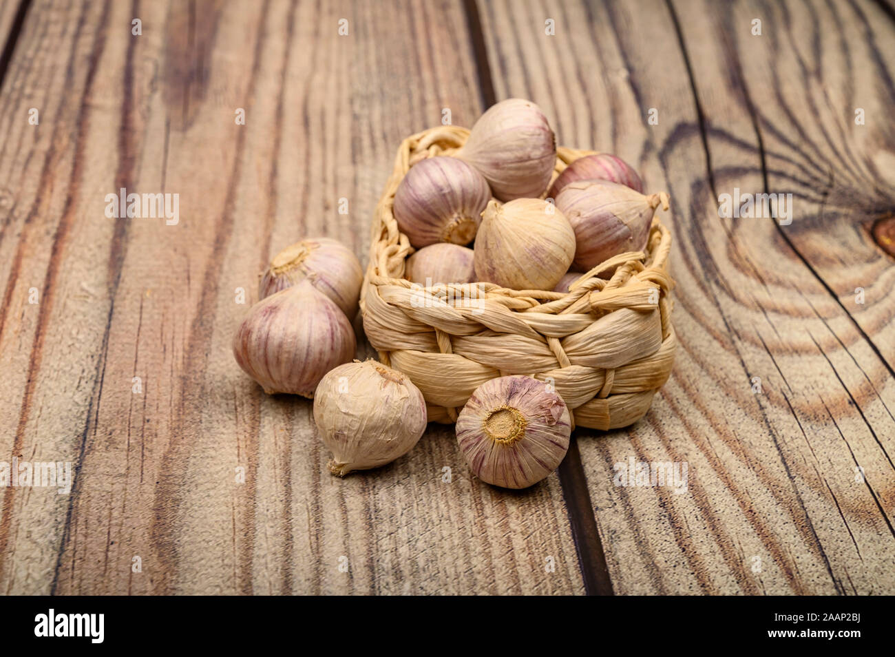 A pochi capi di giovani aglio in un cesto di vimini su un sfondo di legno. Raccolto autunnale. L'agricoltura moderna. Close up Foto Stock
