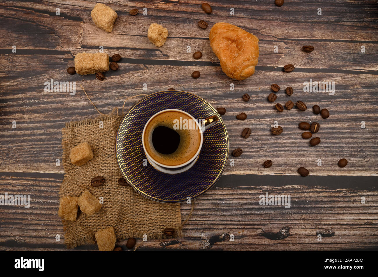 Tazza da caffè, croissant, lo zucchero di canna e i chicchi di caffè su sfondo di legno. Close up Foto Stock