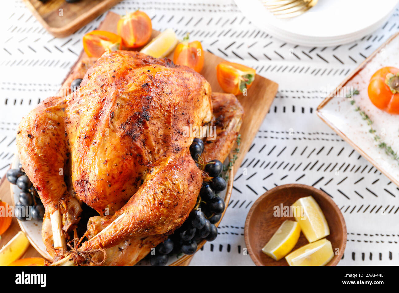 Arrosto di tacchino intero su un tavolo con persimmon, blu uva e limone per la famiglia per la Festa del Ringraziamento. Foto Stock