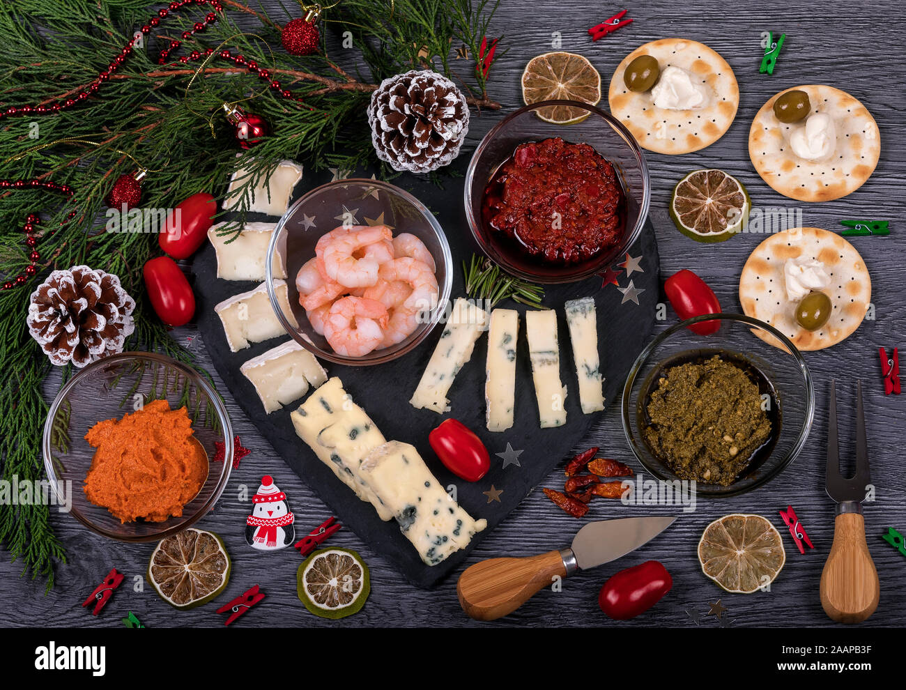 Una oscura un vassoio di formaggi con harissa e pasta al pesto, parmigiano, gorgonzola, rosmarino, olio d'oliva e biscotti. Il cibo italiano con decorazioni di Natale. Foto Stock