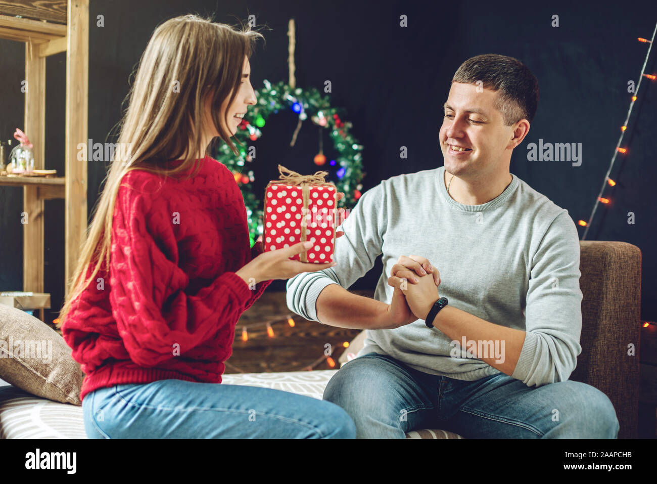 Giovane donna bella moglie dà al marito un regalo a sorpresa box. Una  coppia sposata si festeggia il Natale e il nuovo anno in un accogliente  ambiente domestico Foto stock - Alamy