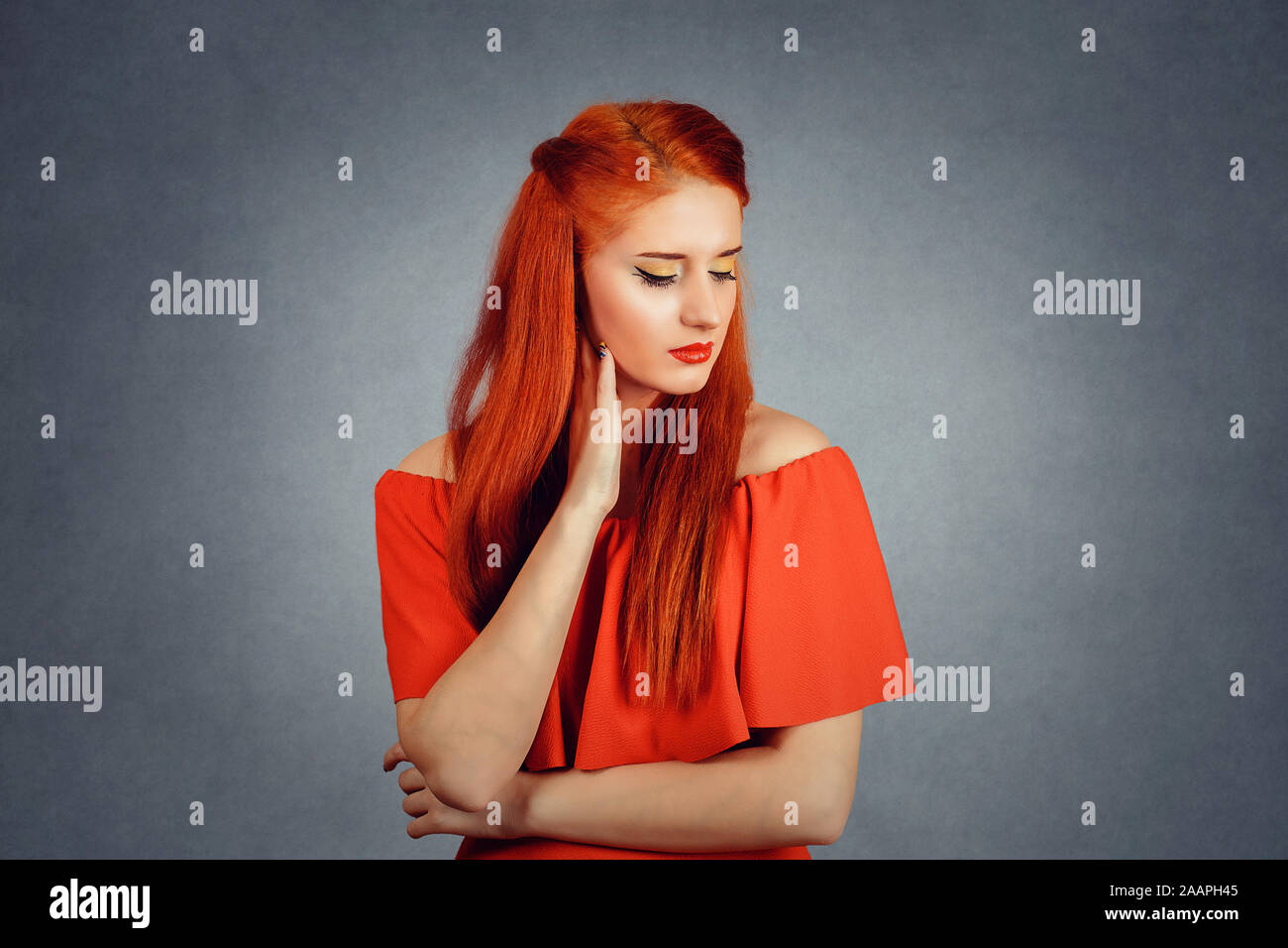 Premuto. Profilo laterale del triste redhead giovane donna in abito rosso guardando in giù con gli occhi chiusi isolati su sfondo grigio Foto Stock